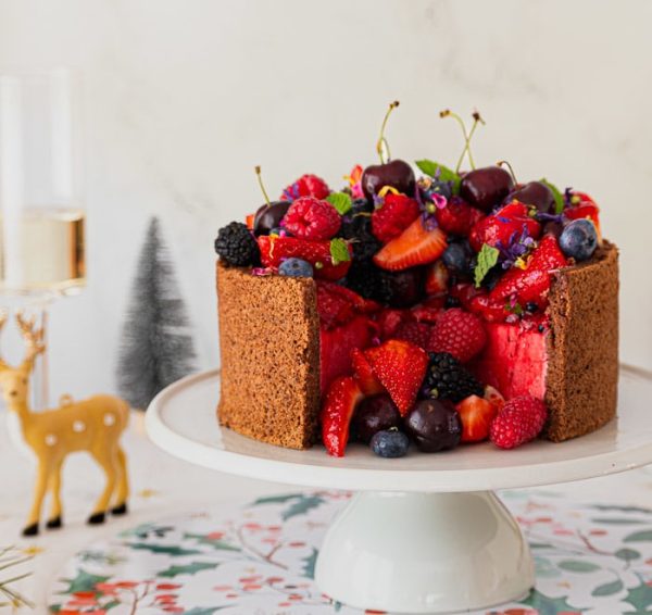 Raspberry Bavarois cake with two portions cut out and mixed berry fruit in cut out section on cake stand with christmas decorations on table