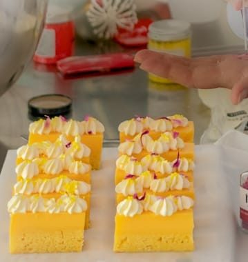 Lemon curd slices being decorated with edible flowers on top. Tweezers taking flowers from hand