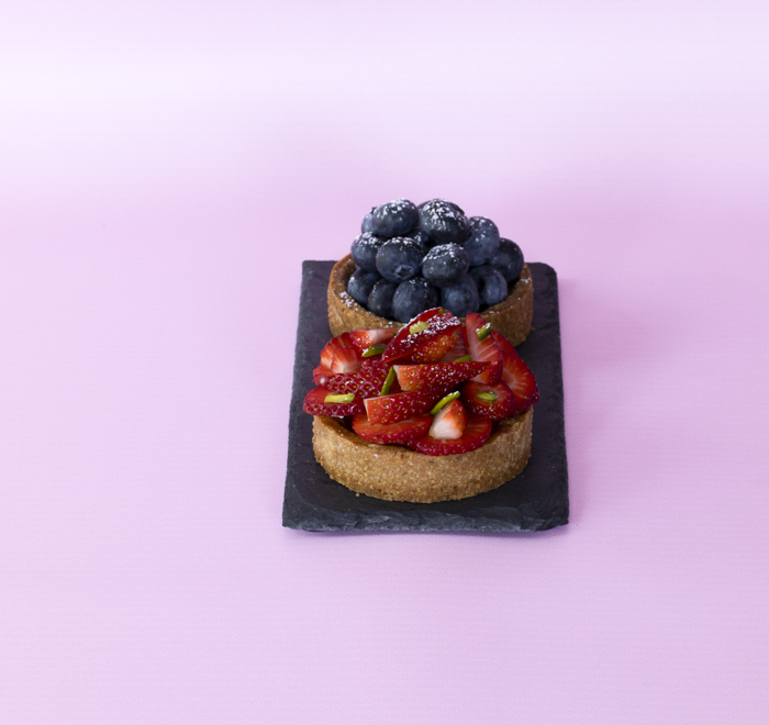 Two tarts- strawberry at the front and blueberry, presented on black slate